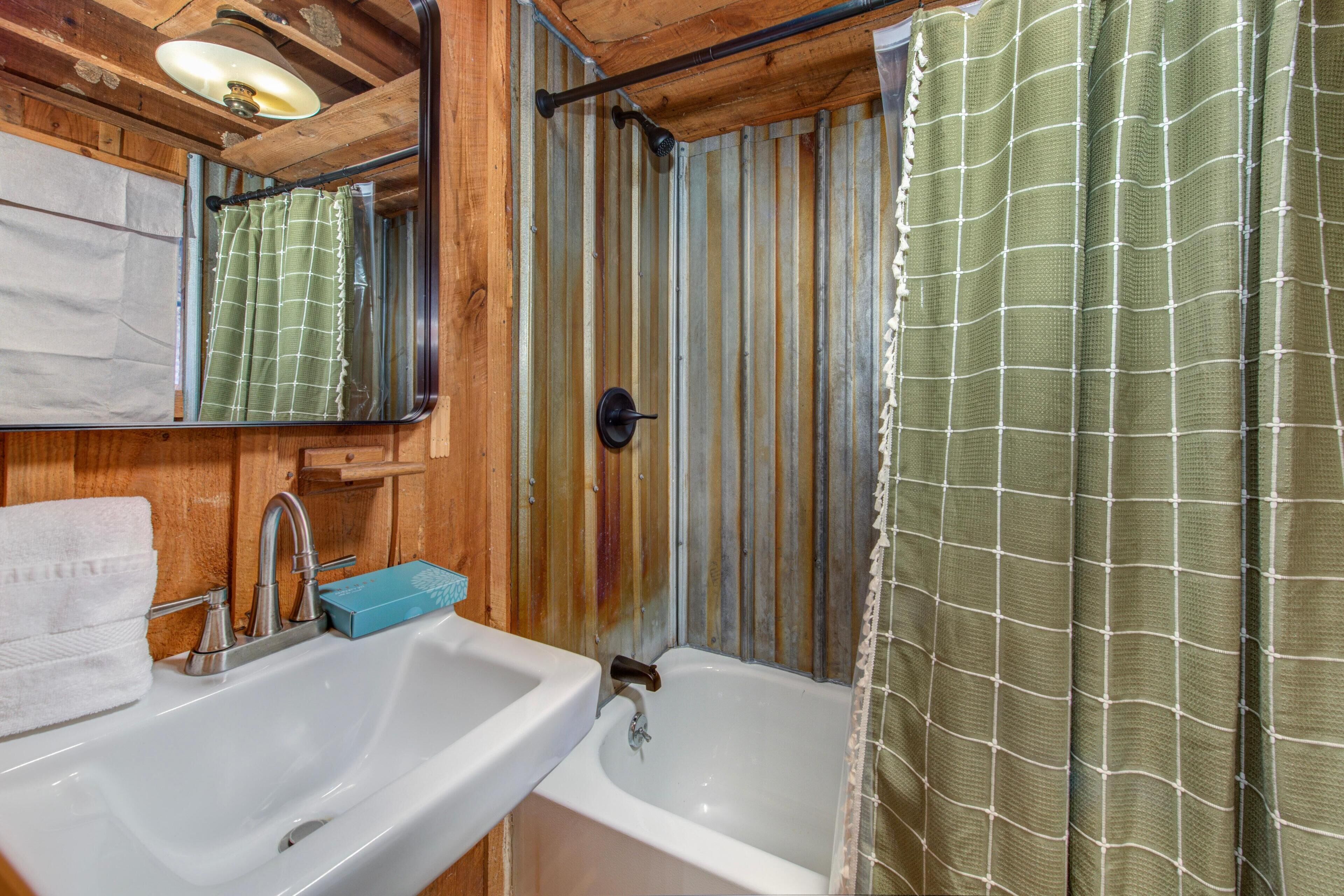 Une salle de bain avec un intérieur en bois, un lavabo blanc, une baignoire, un miroir et un rideau de douche vert.