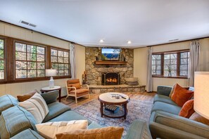 A living room with a stone fireplace, large windows, and a cozy seating area. - Dockside Dreams (Sevierville)