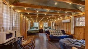 Ein Interieur einer Holzhütte mit Holzwänden, einem Bett, einer Couch, einem Esstisch und einer Mikrowelle.