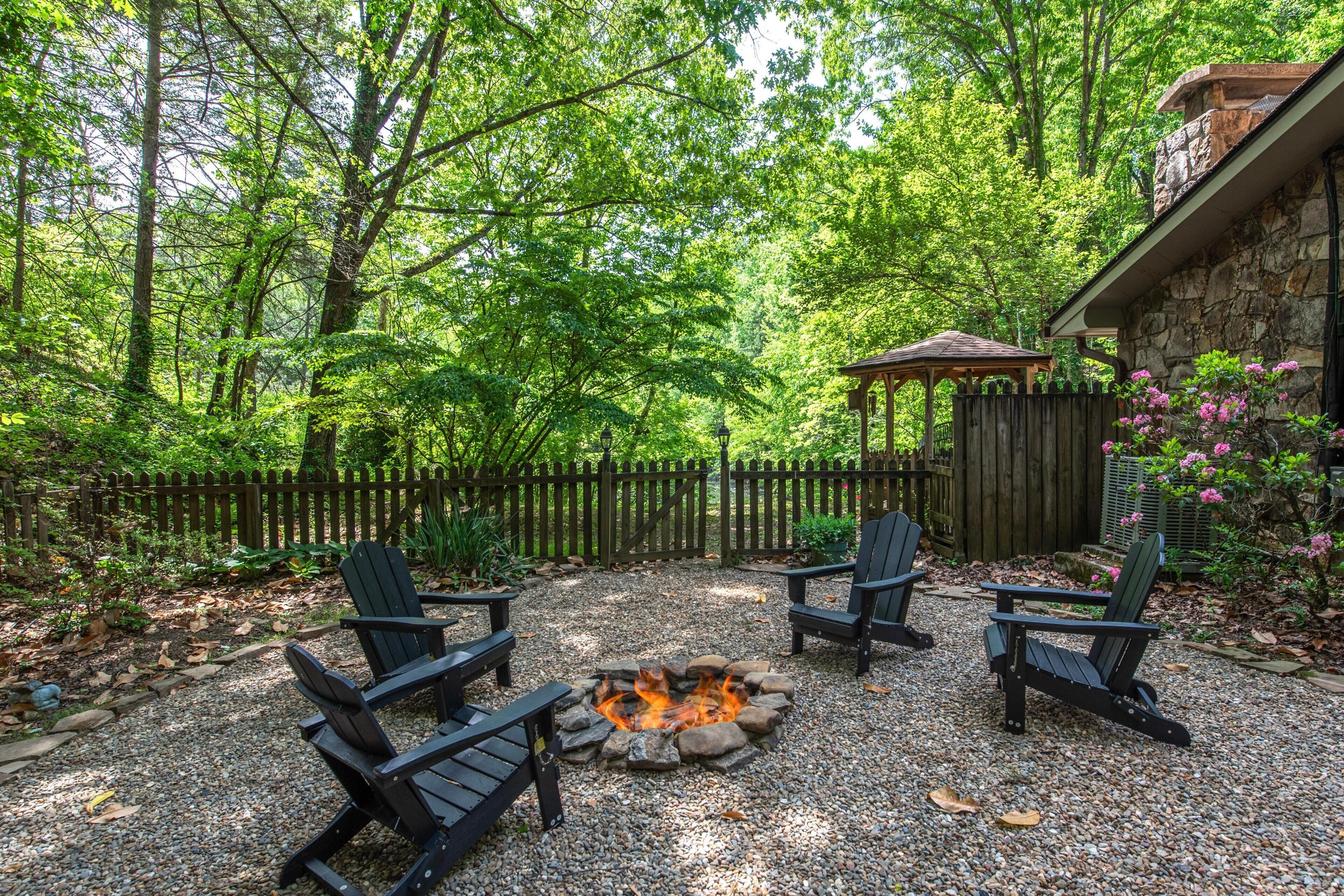 Ein Garten mit Feuerstelle, Adirondack-Stühlen und einem Holzzaun.
