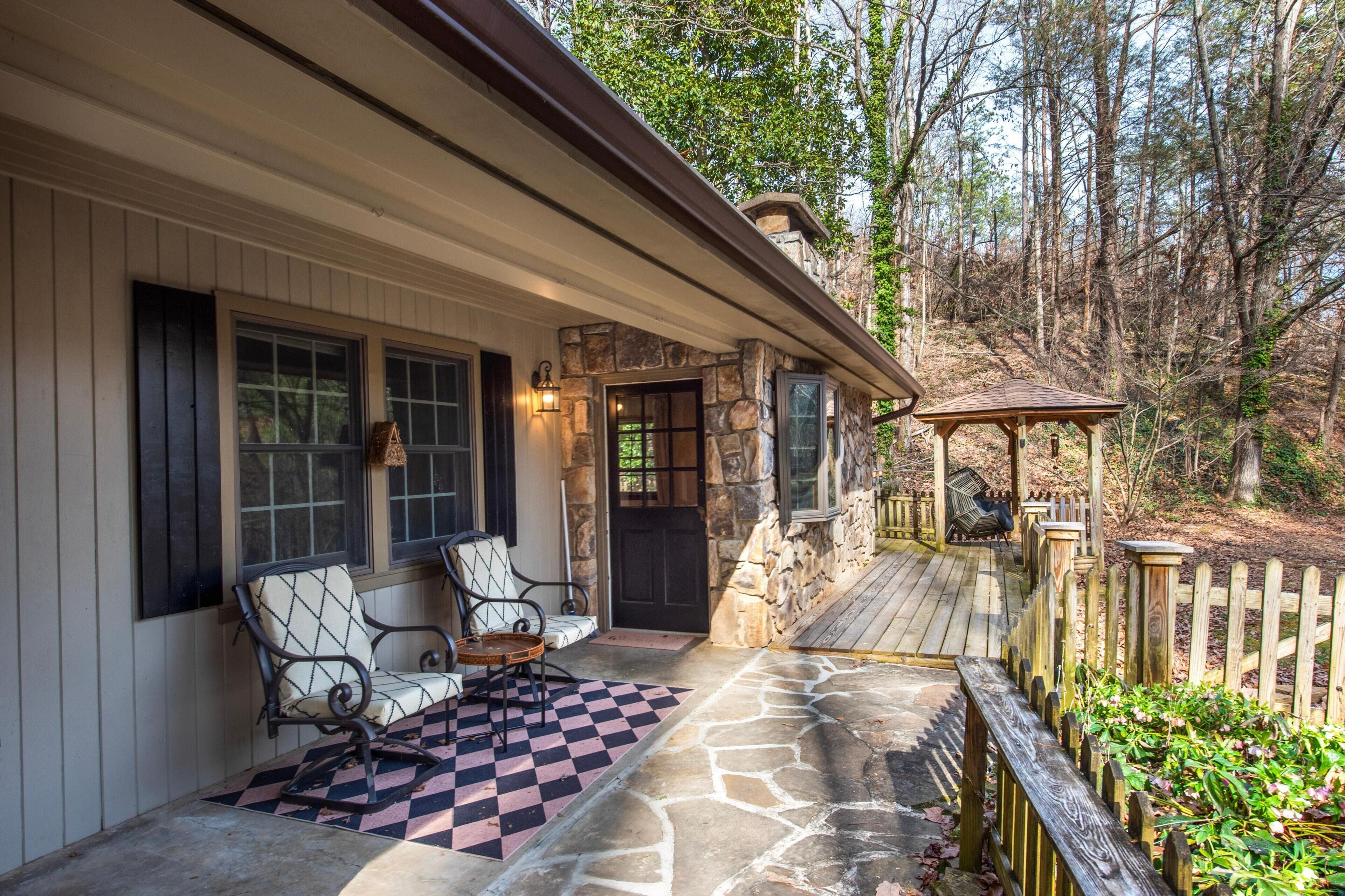 A stone exterior with a porch, two chairs, a table, and a wooden deck.