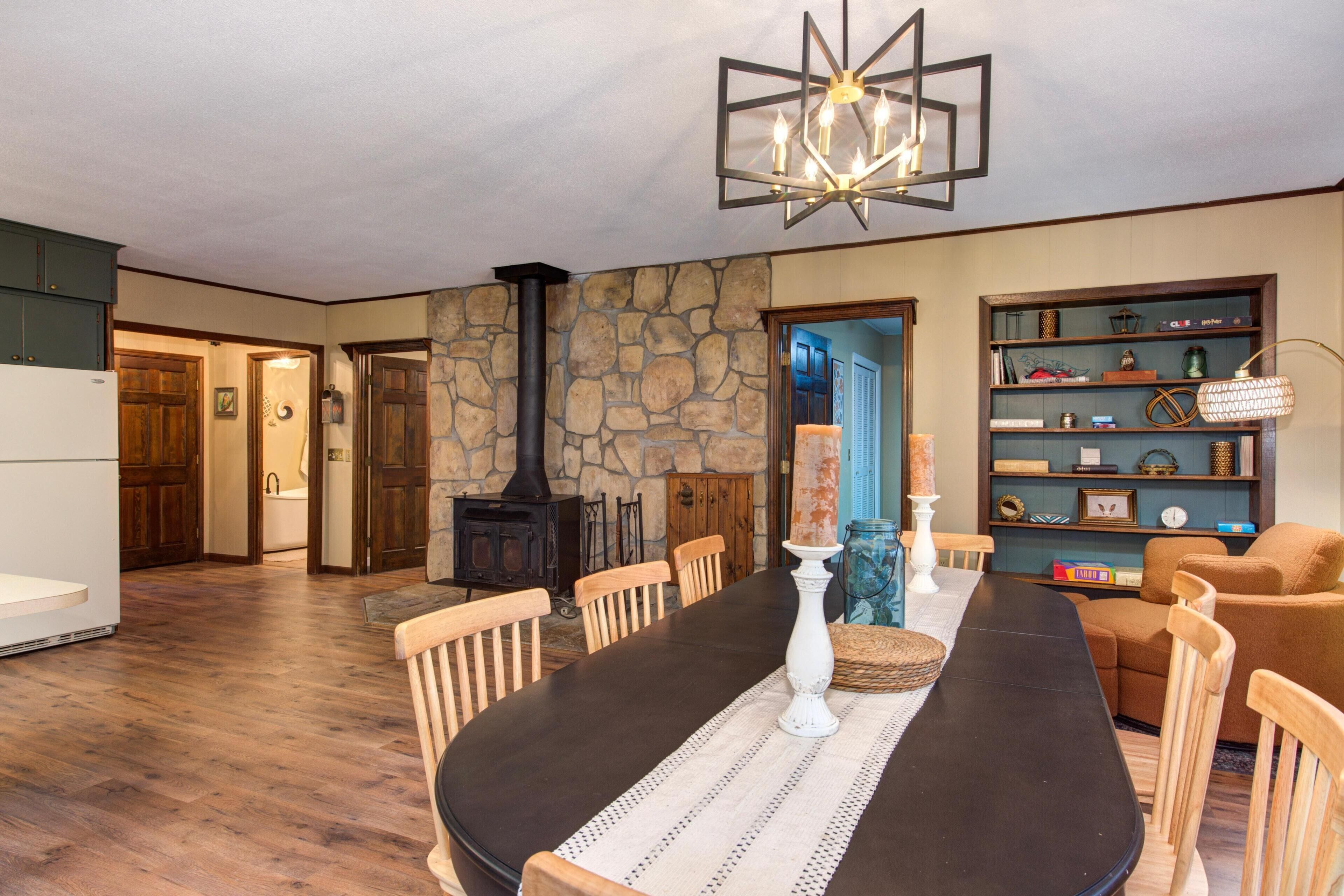 A dining area with a stone wall, a fireplace, wooden chairs, a black table, and a chandelier.