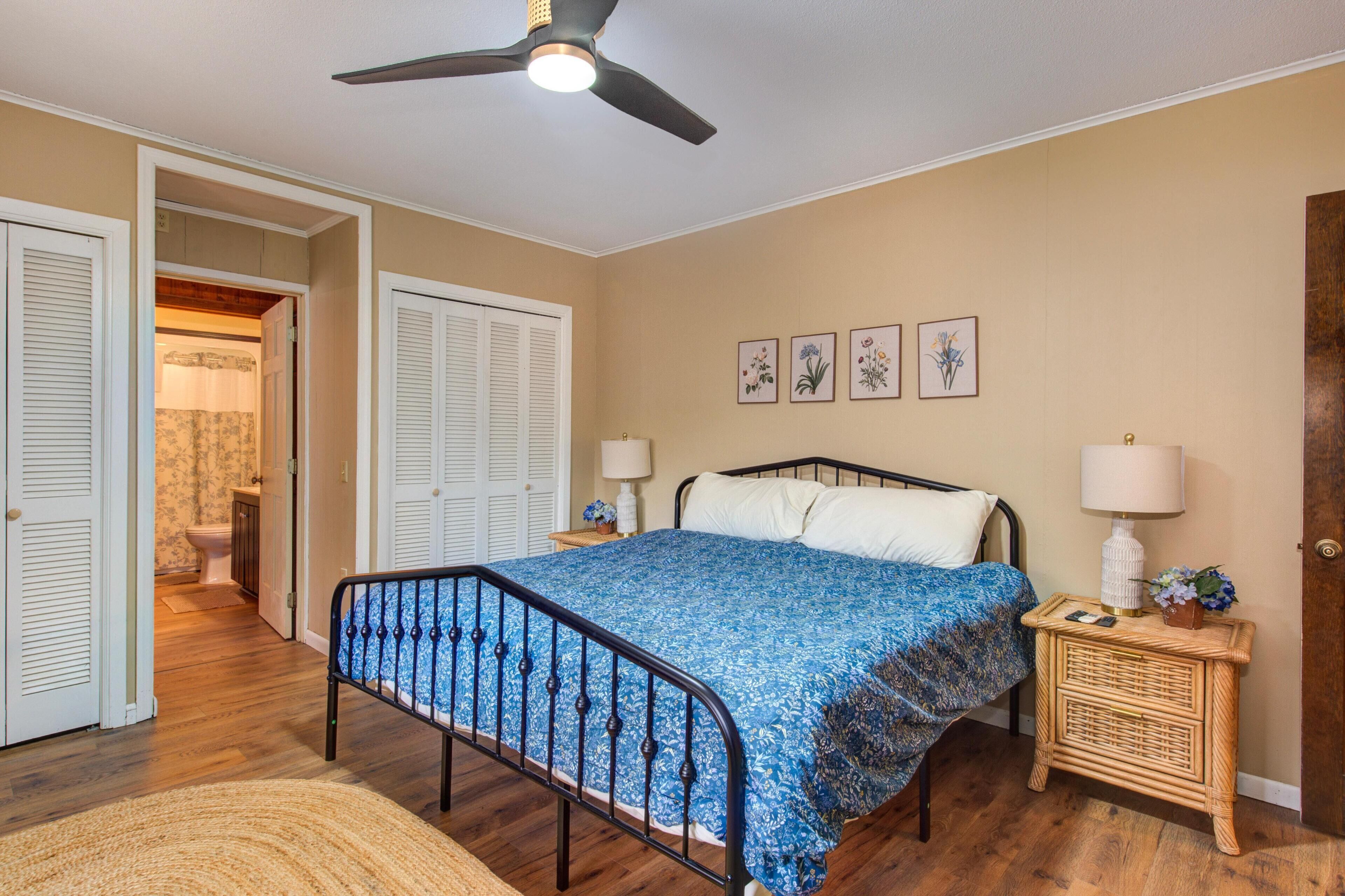 Un dormitorio con cama, mesitas de noche, ventilador de techo y una puerta que da a otra habitación.