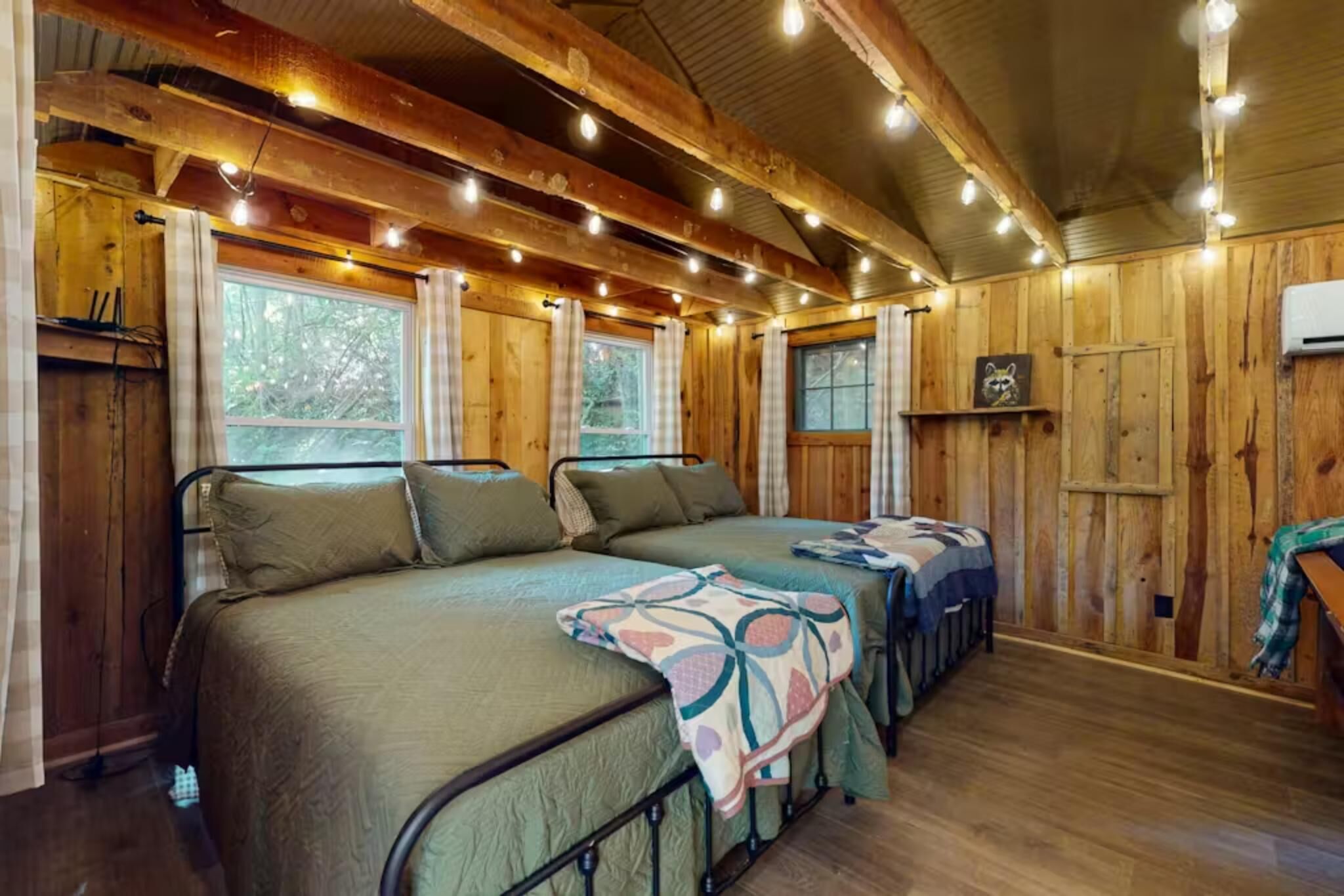 L’intérieur d’une cabane avec deux lits, des murs en bois et des guirlandes lumineuses.