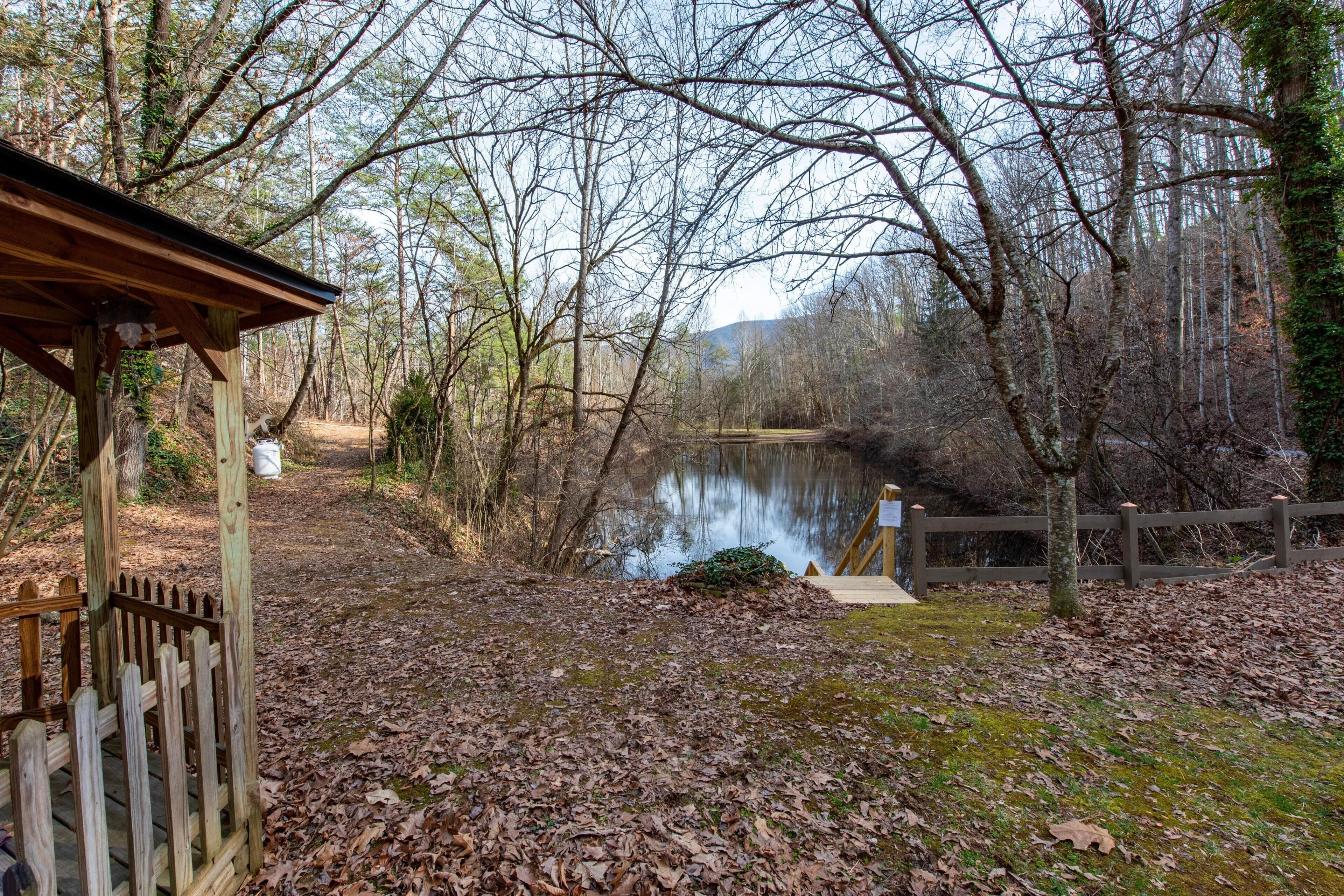 A wooden gazebo, a pond, and a wooden fence in a wooded area.