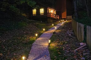 A pathway leading to a wooden building with illuminated windows and a wooden fence. - Dockside Dreams (Sevierville)