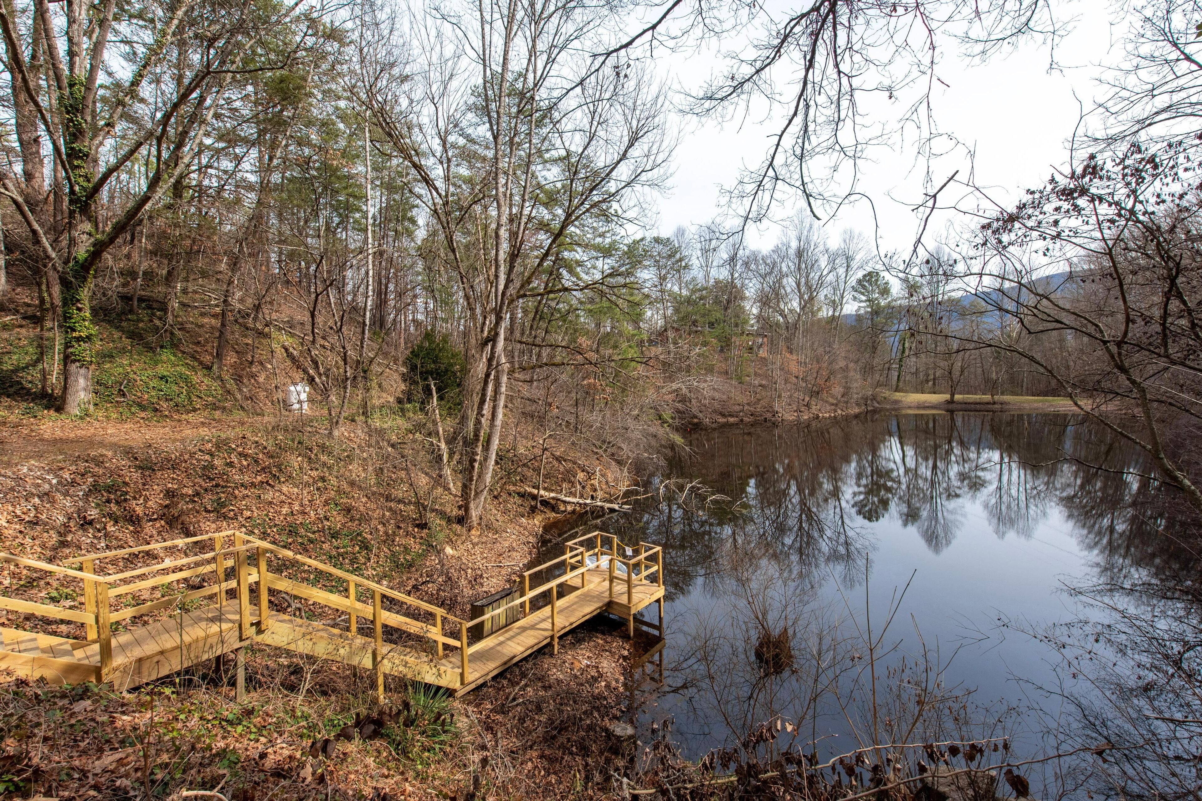 A wooden bridge over a calm body of water, surrounded by trees and a forested area.