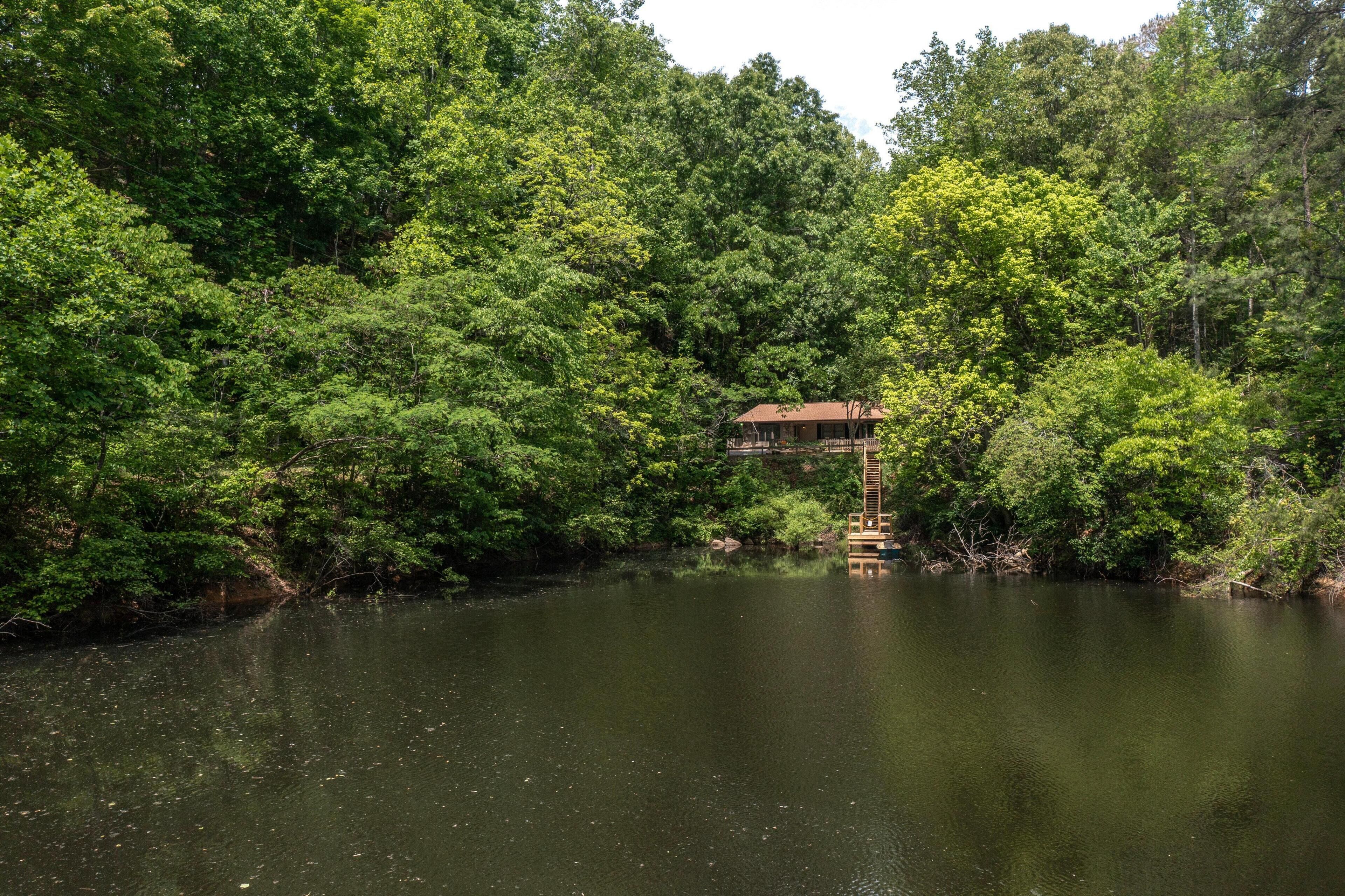 A house surrounded by dense forest and a calm body of water.