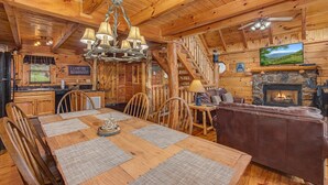 L’intérieur d’une cabane comprend un coin repas, une cheminée, un téléviseur et des murs en bois.