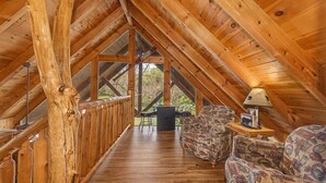Un intérieur en bois avec un plafond haut, une rambarde en bois, un canapé et une table avec une lampe.