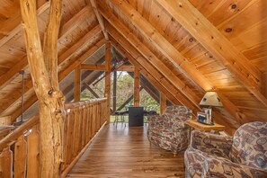 A wooden interior with a high ceiling, a wooden railing, a sofa, and a table with a lamp. - Gods Grace (Pigeon Forge)