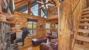 L'intérieur d'une cabane en rondins, avec une cheminée, un canapé en cuir et un ventilateur de plafond.