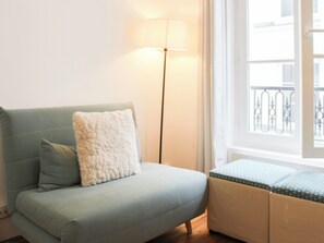 Ein hellblaues Sofa mit einem flauschigen Kissen und passendem Hocker, eine Stehlampe und ein Fenster mit Blick auf einen Balkon.