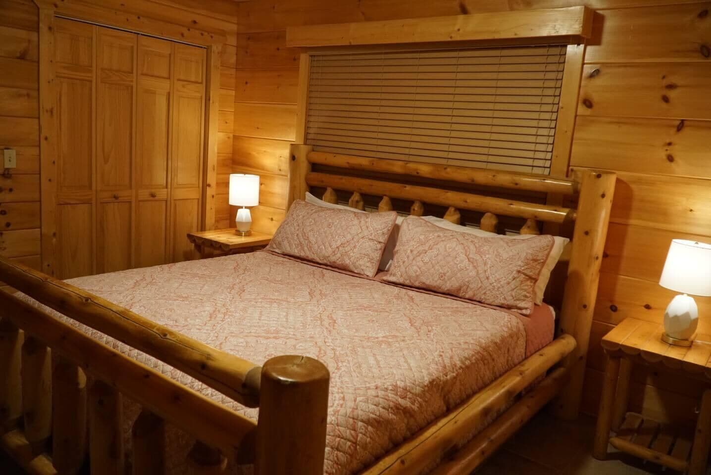 Un lit en bois avec un couvre-lit matelassé, deux lampes de chevet et une fenêtre avec des stores.