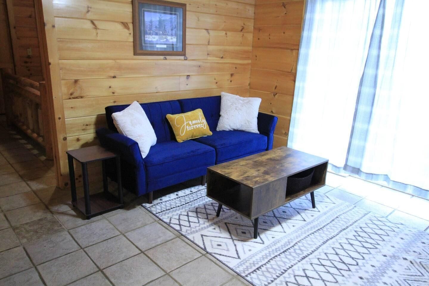 A wooden cabin interior with a blue sofa, a small table, and a patterned rug.