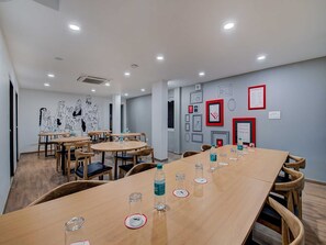 Une salle de conférence équipée de tables rondes, de chaises et d’une longue table sur laquelle sont disposées des bouteilles d’eau et des verres.