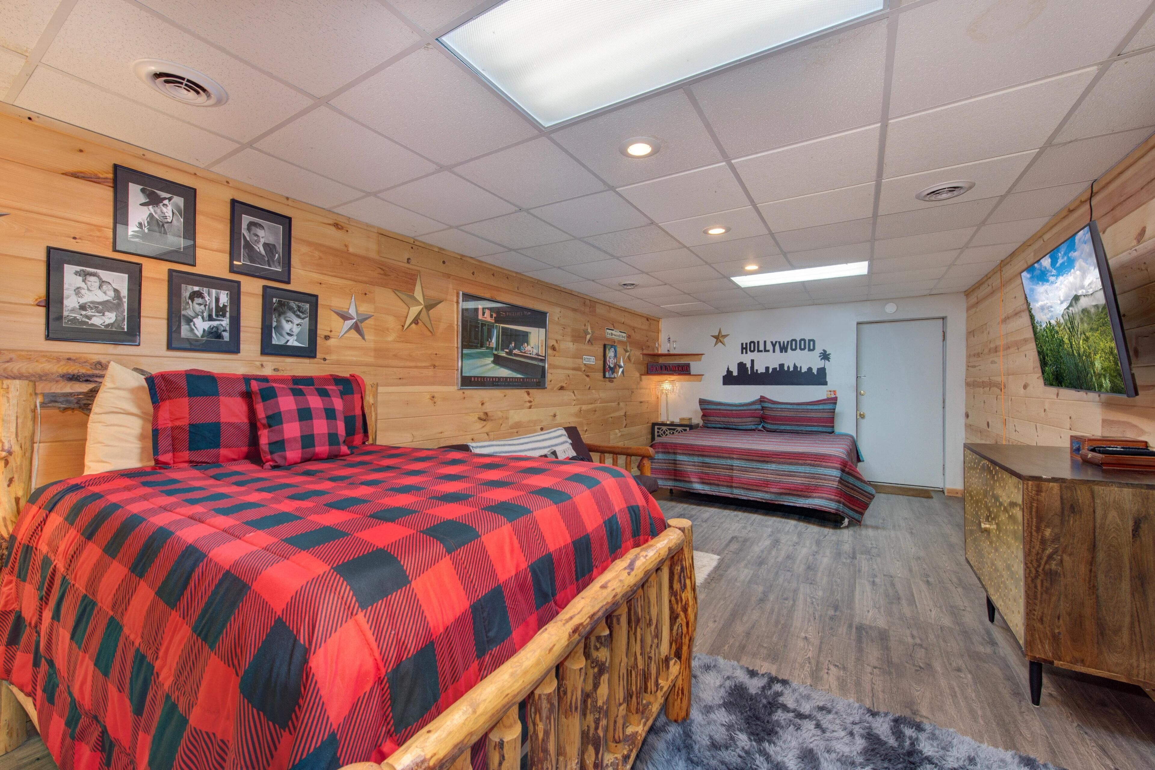 Une pièce avec un mur en bois, un lit recouvert d’une couverture à carreaux rouges et noirs, un deuxième lit avec une literie à rayures, une commode en bois et une décoration en forme d’étoile sur le mur.