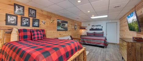 Une pièce avec un mur en bois, un lit recouvert d’une couverture à carreaux rouges et noirs, un deuxième lit avec une literie à rayures, une commode en bois et une décoration en forme d’étoile sur le mur.