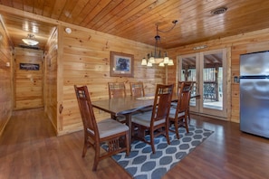 A wooden cabin interior with a dining table, chairs, a chandelier, and a refrigerator. - Country Cabin in the City (Pigeon Forge)