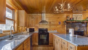 A wooden cabin interior with a kitchen featuring granite countertops, a stove, and a sink. - Country Cabin in the City (Pigeon Forge)