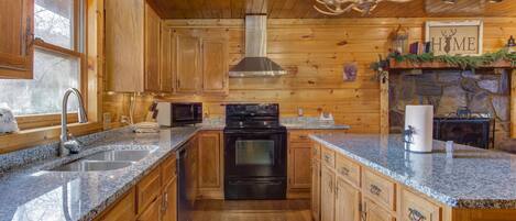 A wooden cabin interior with a kitchen featuring granite countertops, a stove, and a sink.