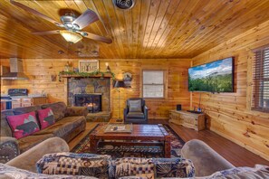A log cabin interior with a fireplace, a television, a ceiling fan, and a cozy seating area. - Country Cabin in the City (Pigeon Forge)