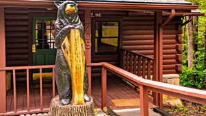 A bear statue on a wooden stump in front of a log cabin with a green door and a number '709' on the wall. - Country Cabin in the City (Pigeon Forge)