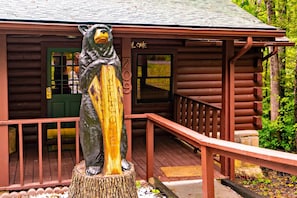 A bear statue on a wooden stump in front of a log cabin with a green door and a number '709' on the wall. - Country Cabin in the City (Pigeon Forge)