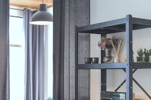Ein Zimmer mit einer Metallregaleinheit, einer Pendelleuchte und einem Fenster mit Vorhängen.
