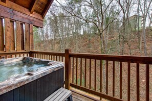 Eine Holzterrasse mit Whirlpool, umgeben von bewaldeter Landschaft.