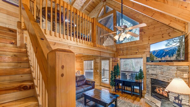 Interior em madeira com escada, lareira, sofá e televisão.