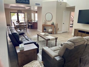 Ein Wohnzimmer mit einer Couch, Sesseln, einem Couchtisch und einem an der Wand befestigten Fernseher.