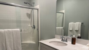 A bathroom with a shower, toilet, sink, and a mirror.