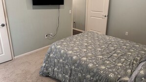 A bedroom with a bed, a television mounted on the wall, and a door leading to another room.