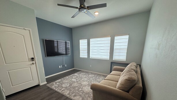 A living room with a ceiling fan, a flat-screen TV mounted on the wall, and a beige sofa.