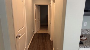 A narrow hallway with wooden flooring and white doors, leading to a room with a visible door.