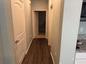 Un couloir étroit, doté d’un plancher en bois et de portes blanches, qui mène à une pièce dont on aperçoit la porte.