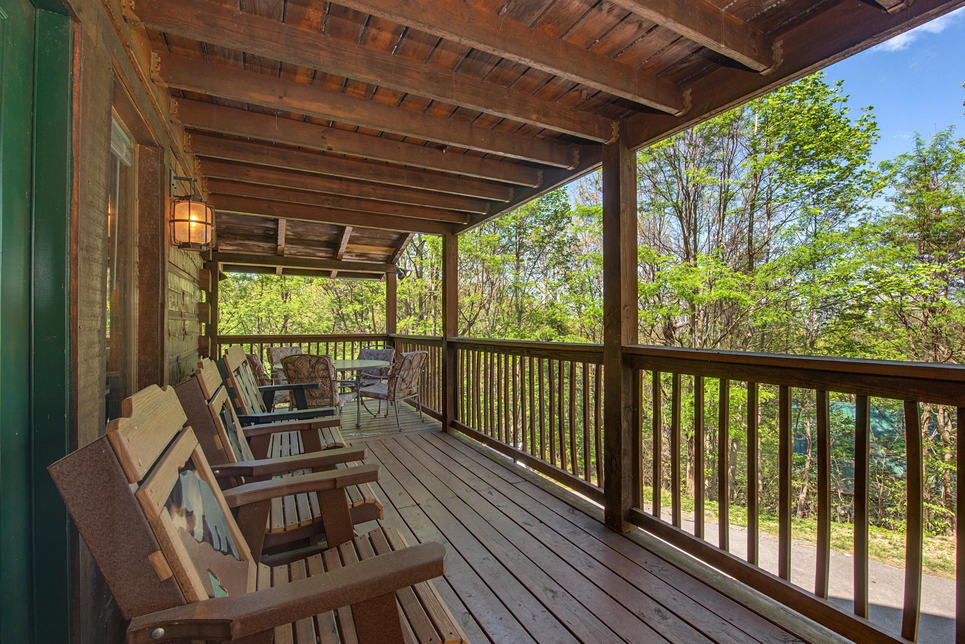 A wooden deck with benches and a table, surrounded by a railing, overlooking a forested area.