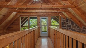 A wooden interior with a stone wall, wooden railings, and a door leading outside. - Hilltop Bearadise (Gatlinburg)