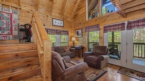 A wooden cabin interior with a staircase, two leather sofas, a table, and plaid curtains. - Hilltop Bearadise (Gatlinburg)