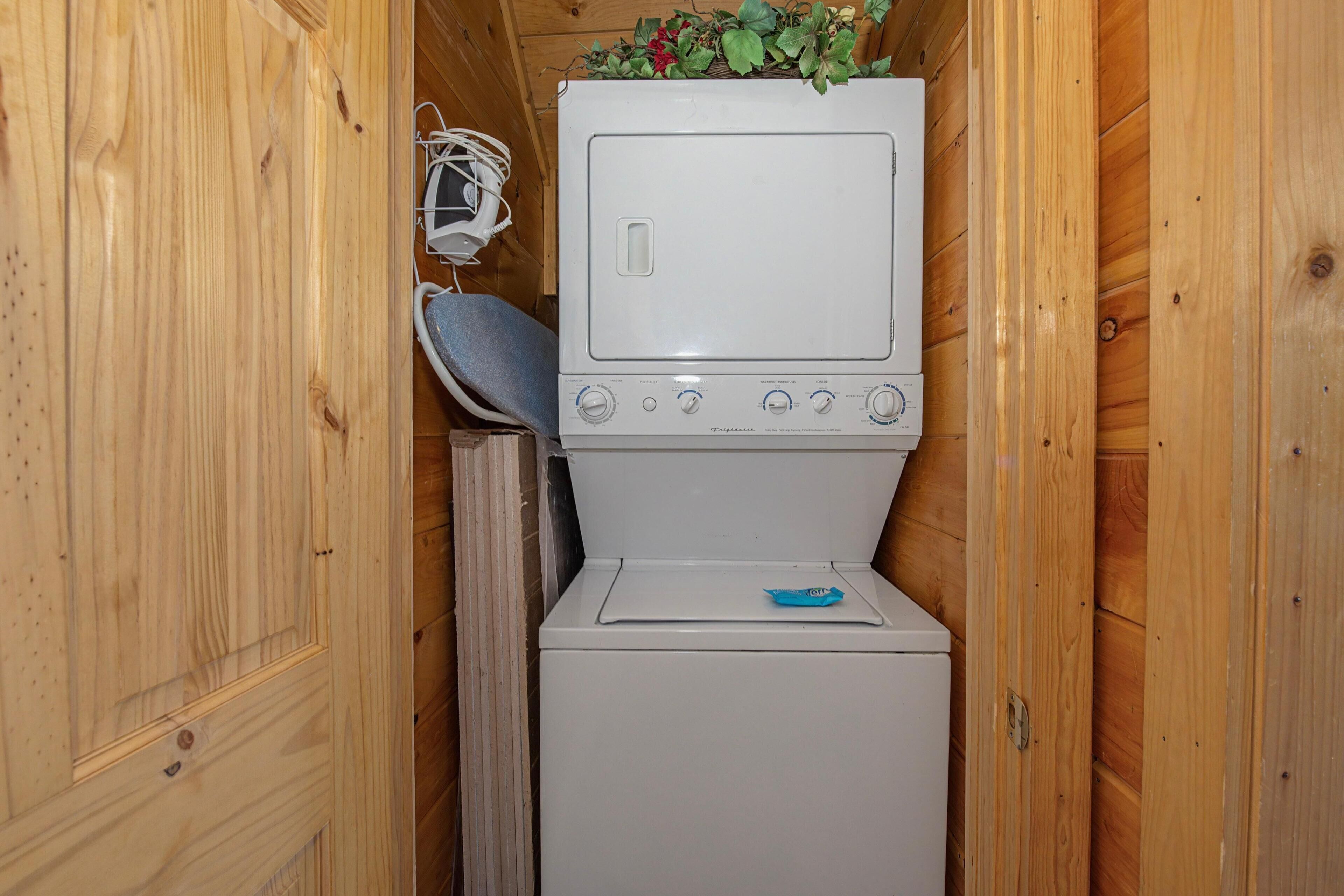 A compact laundry room with a washer and dryer, wooden walls, and a small shelf with plants.