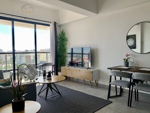 Una sala de estar moderna con un ventanal grande, un televisor de pantalla plana, un comedor y una planta en maceta.