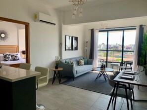 Een moderne woonkamer met een bed, bank, eethoek en grote ramen met uitzicht op de stad.