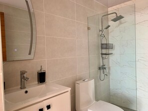 Een moderne badkamer met een douchecabine van glas, een wit wastafelmeubel en een toilet.