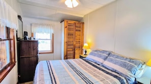 Un dormitorio con cama, mesita de noche con lámpara, armario y ventana con cortinas.
