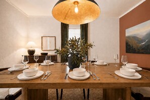 A dining room with a wooden table set for a meal, a vase with flowers, and a painting on the wall.