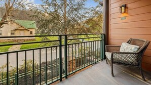 Un balcone con una sedia in vimini e una lanterna, vista su una strada e degli alberi.