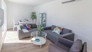 Una sala moderna con un sofá gris, una mesa de centro redonda de vidrio y una silla blanca.
