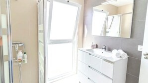 Un baño moderno con cabina de ducha de vidrio, un lavabo blanco y un espejo.