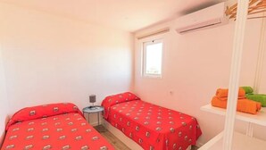 Una habitación pequeña con dos camas, una ventana, una mesa y un estante con toallas.